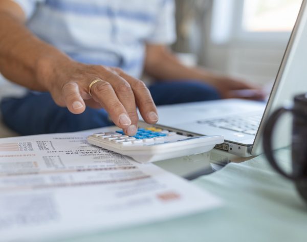 serious-elder-senior-greyhaired-grandpa-using-calculator-counting-bank-loan-payment-holding-papers-home-focused-mature-old-man-doing-paperwork-calculating-bills-managing-finances-sit-sofa-min